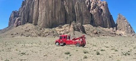 A red tow truck is parked in the middle of a desert in front of a mountain.