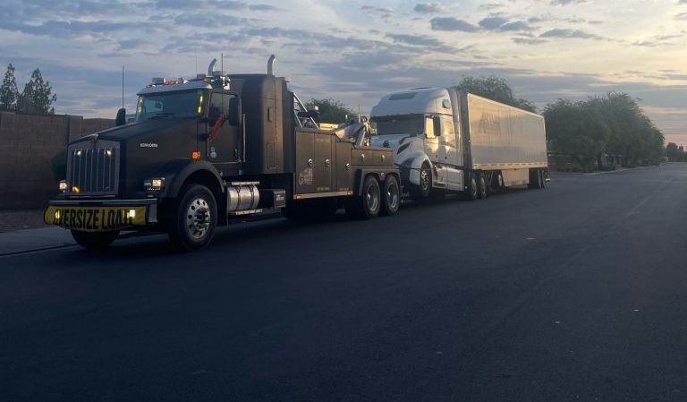 A tow truck is towing a semi truck down a road.