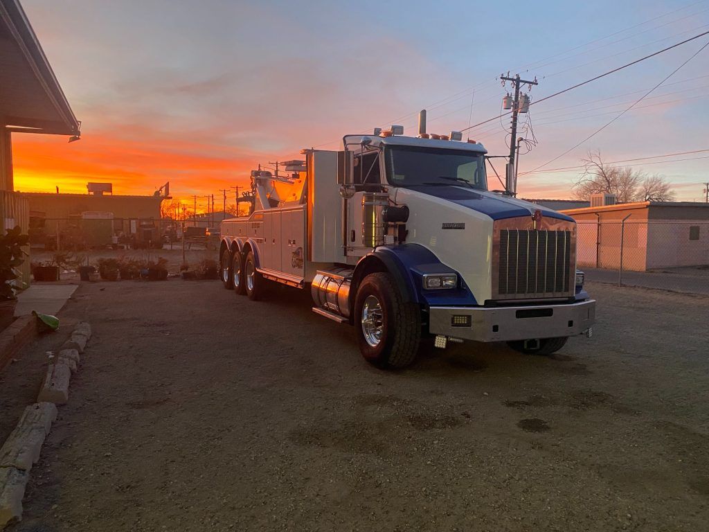 A blue and white tow truck is parked in a parking lot at sunset.