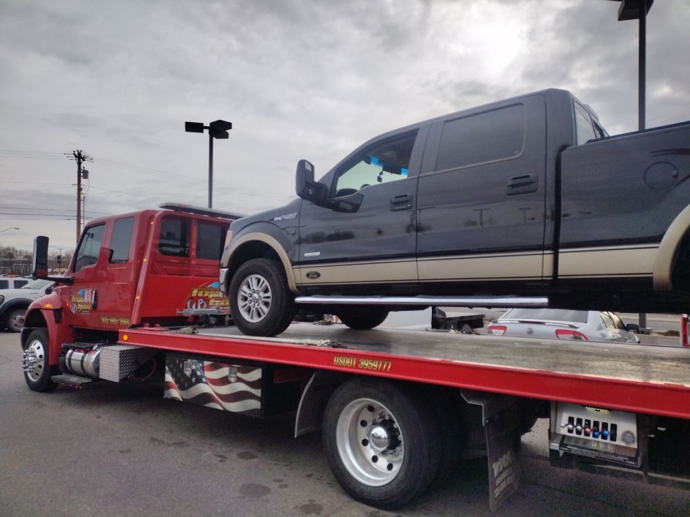 A black truck is sitting on top of a red tow truck.