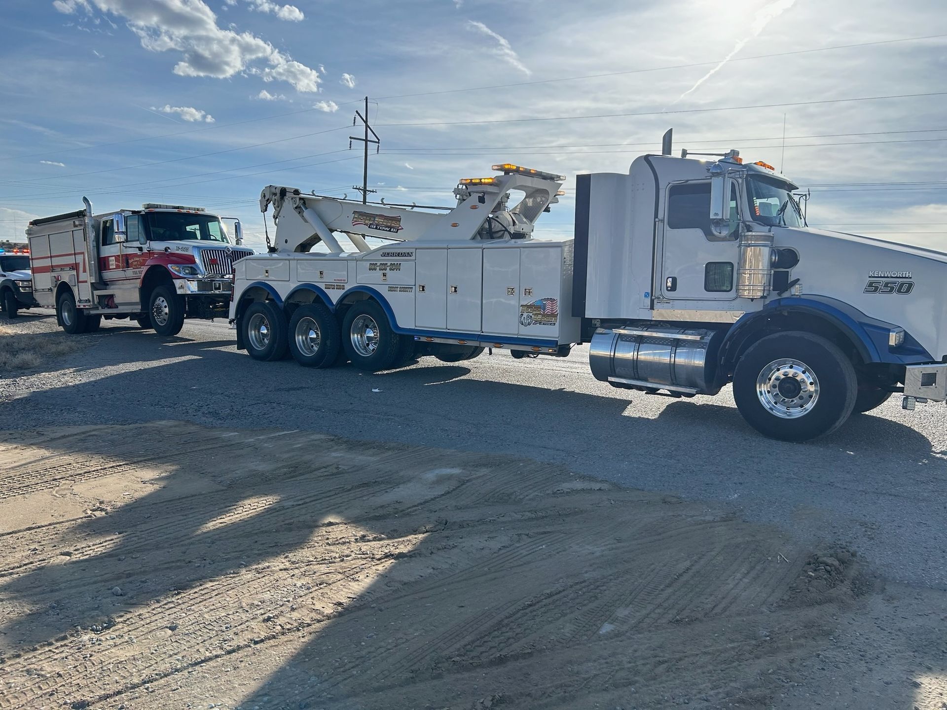 Two tow trucks are parked next to each other on a dirt road.