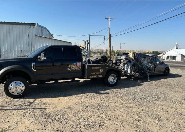 A black tow truck is towing a car and a motorcycle.