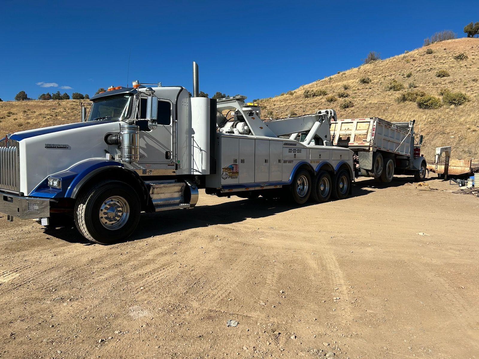 A tow truck is parked in a dirt lot next to a hill.