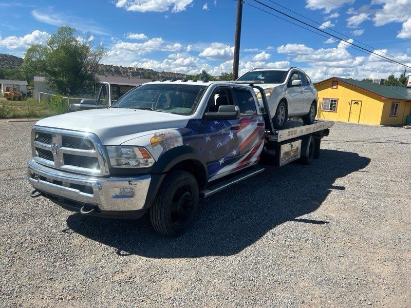 A tow truck with a car on the back is parked in a gravel lot.