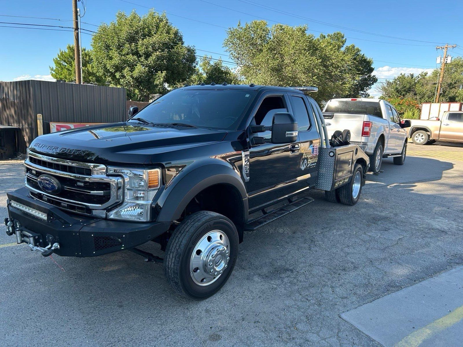 A black ford truck is parked in a parking lot next to a white truck.
