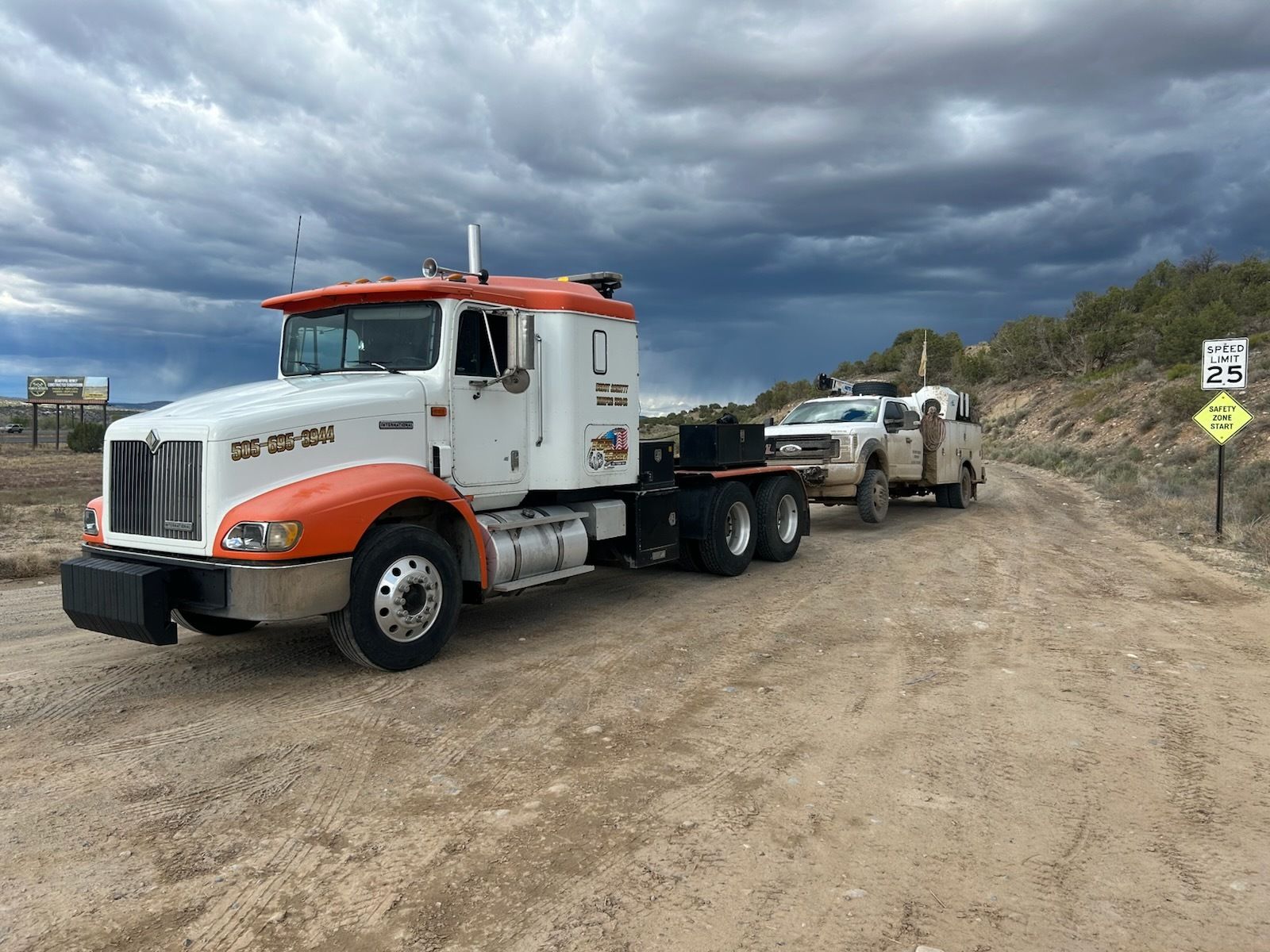Two semi trucks are parked on a dirt road.