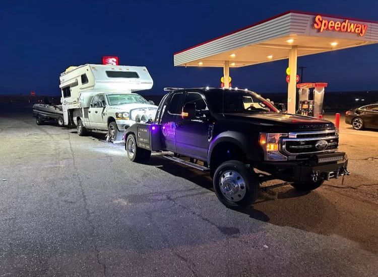 A truck is towing a trailer at a speedway gas station.
