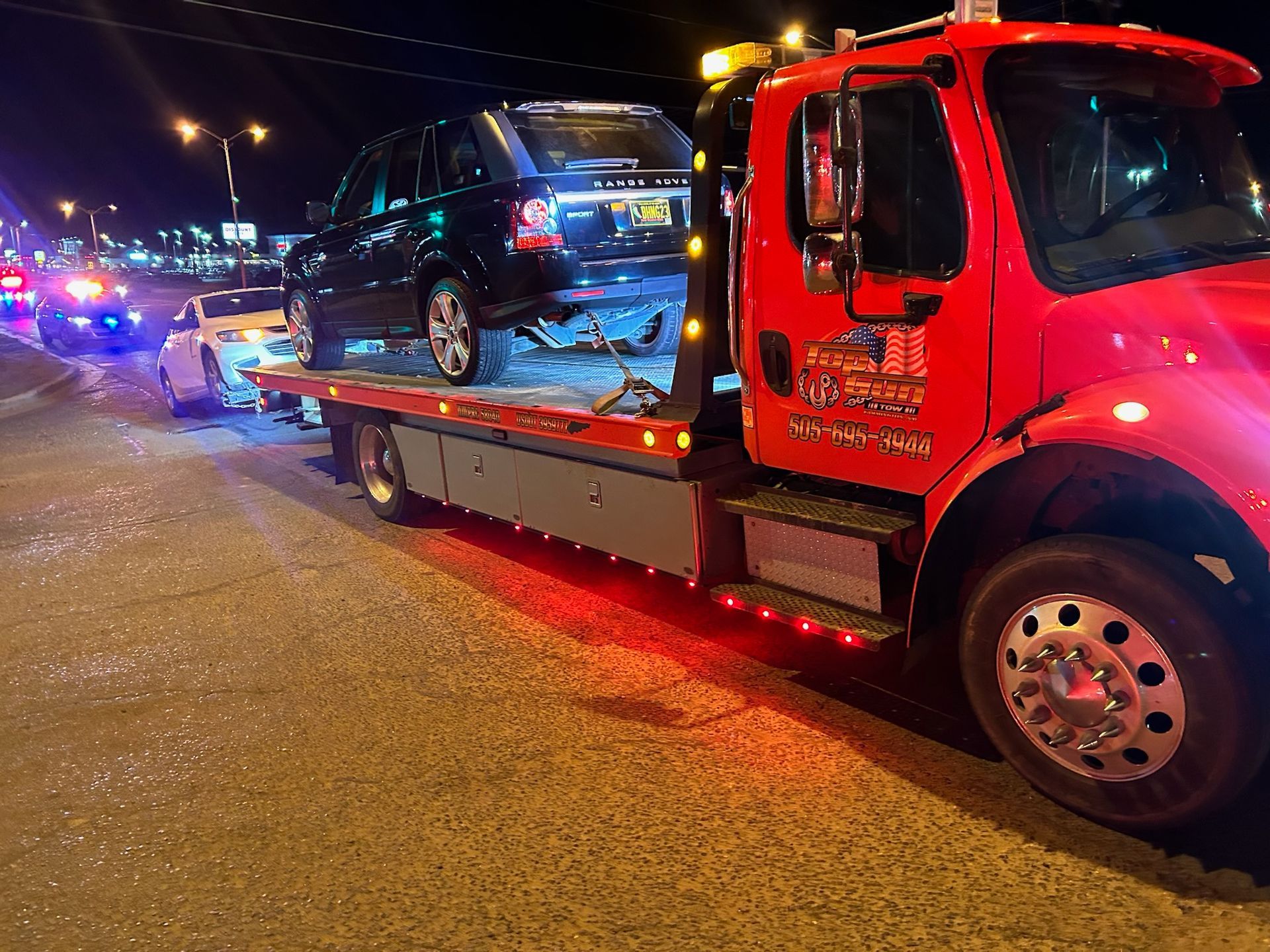 A red tow truck is carrying a car on the back of it.