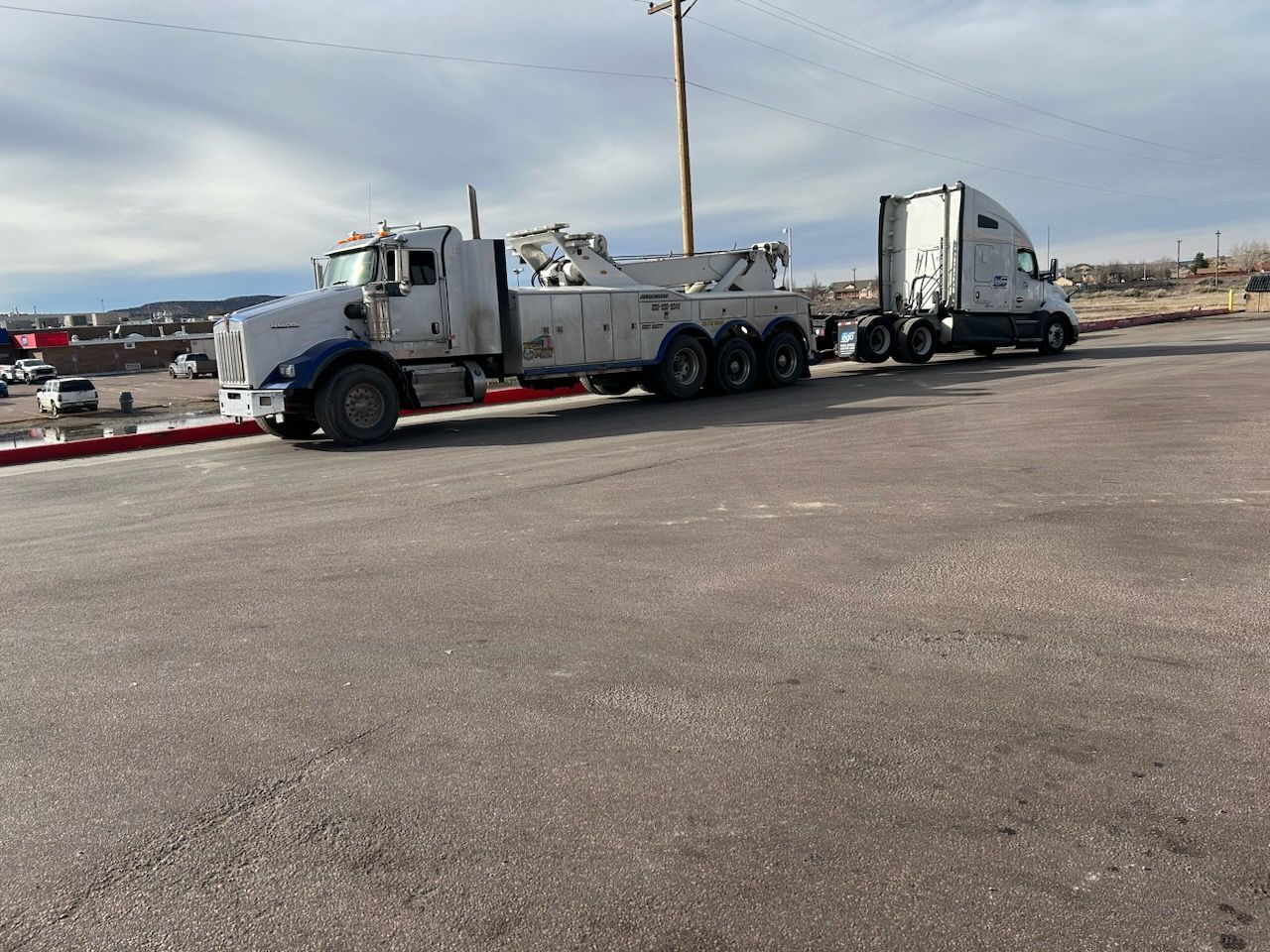 A tow truck is parked next to a semi truck in a parking lot.