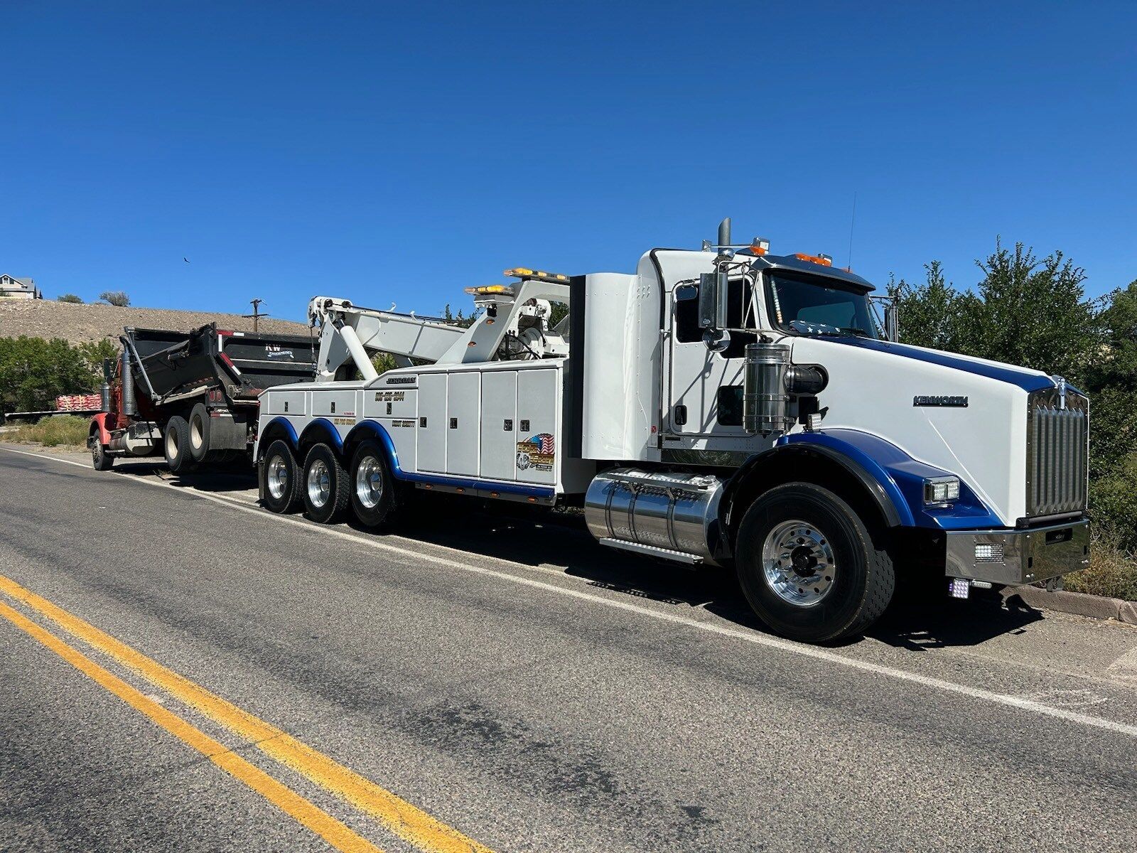 A tow truck is towing a dump truck down the road.
