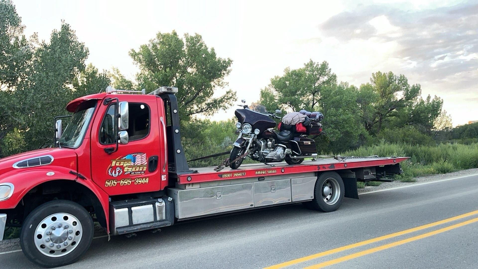 A red tow truck is carrying a motorcycle on the back of it.