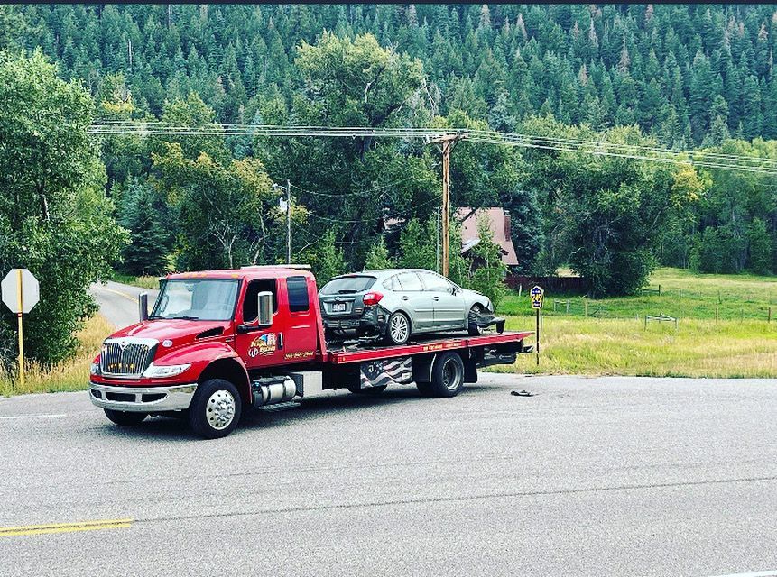 A red tow truck is carrying a car on the back of it.