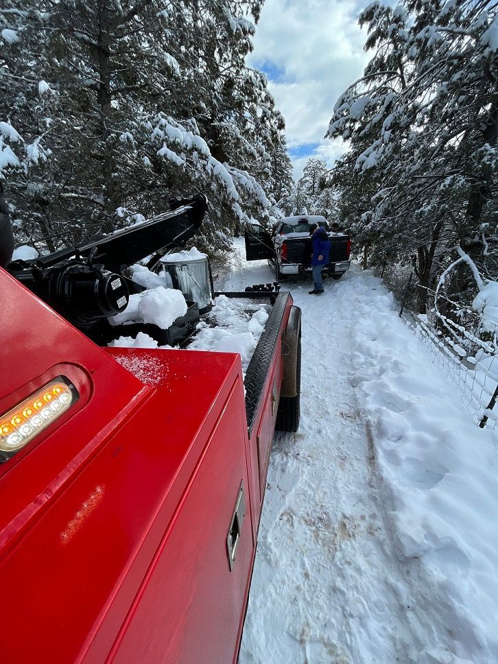 A red tow truck is driving down a snowy road.