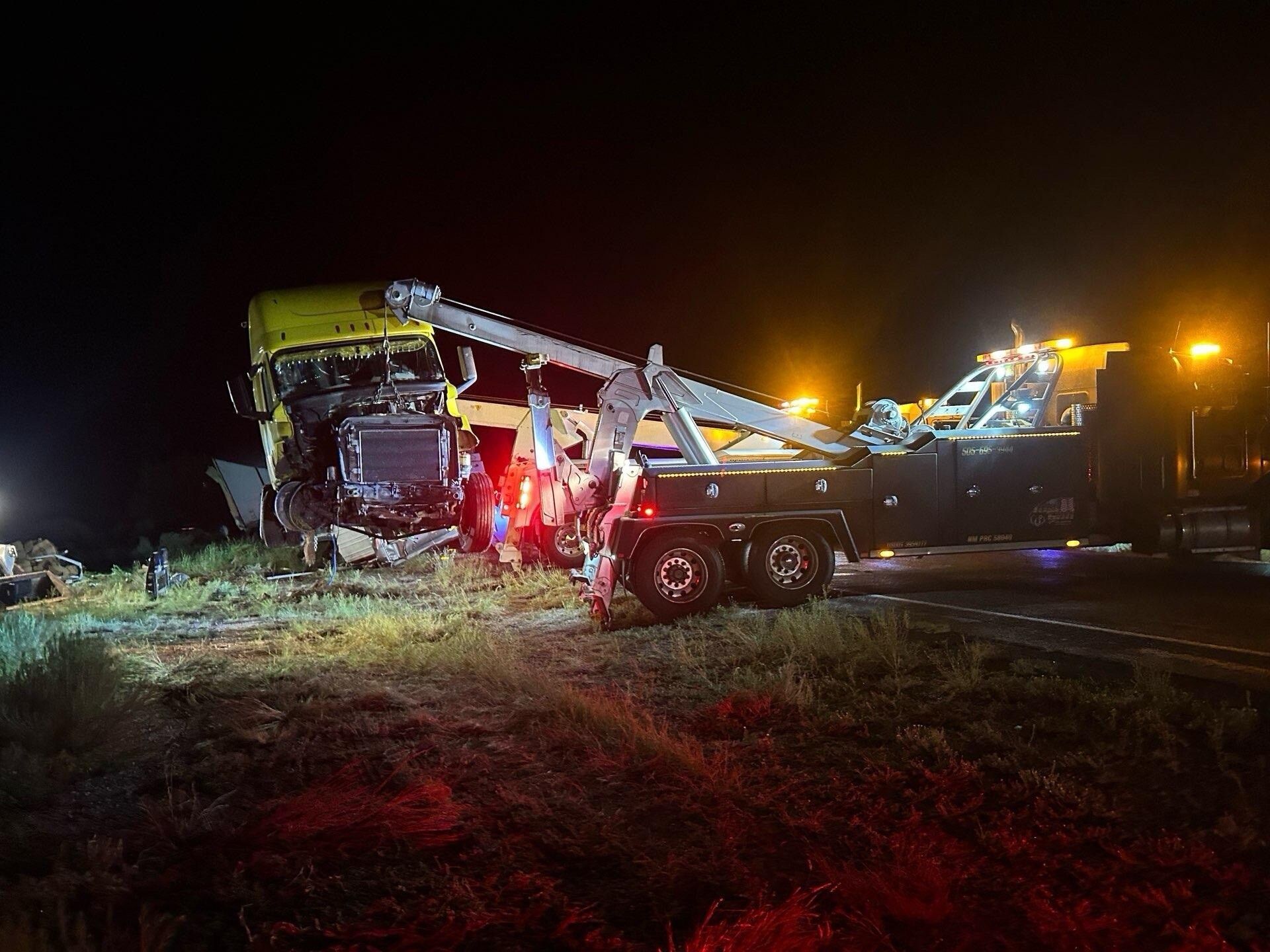 A tow truck is towing a truck that has crashed on the side of the road at night.