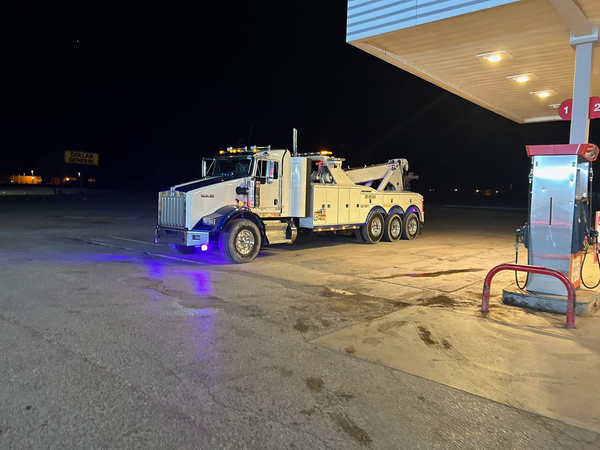 A tow truck is parked in front of a gas station at night.