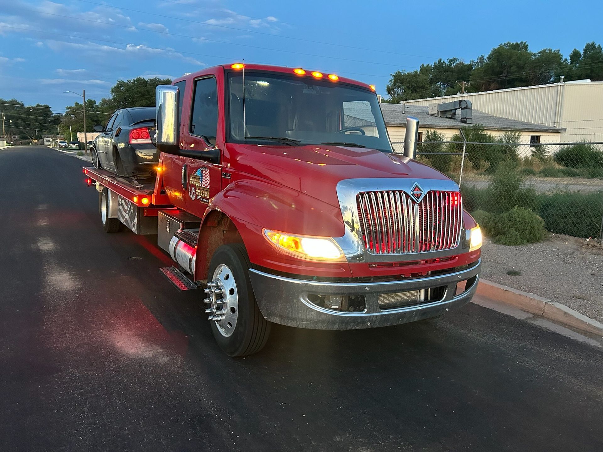 A red tow truck with a car on the back is parked on the side of the road.