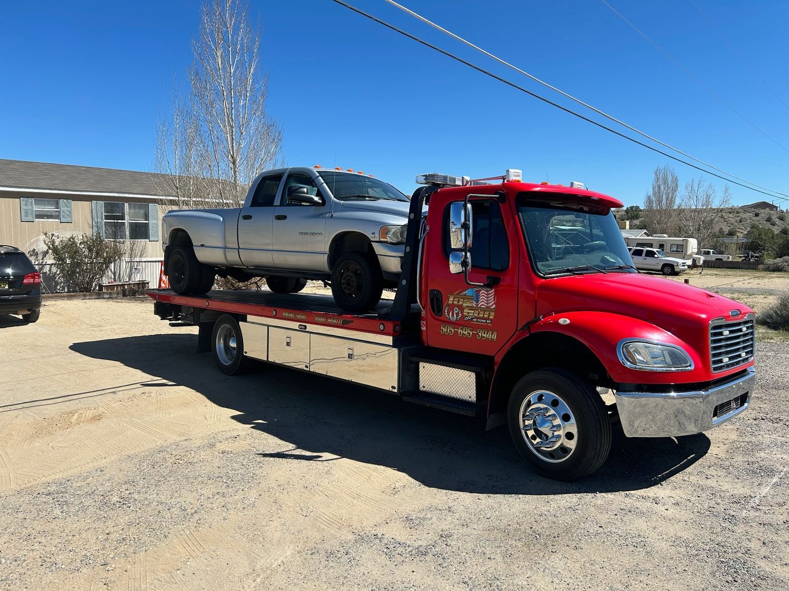 A red tow truck is carrying a silver truck on the back of it.