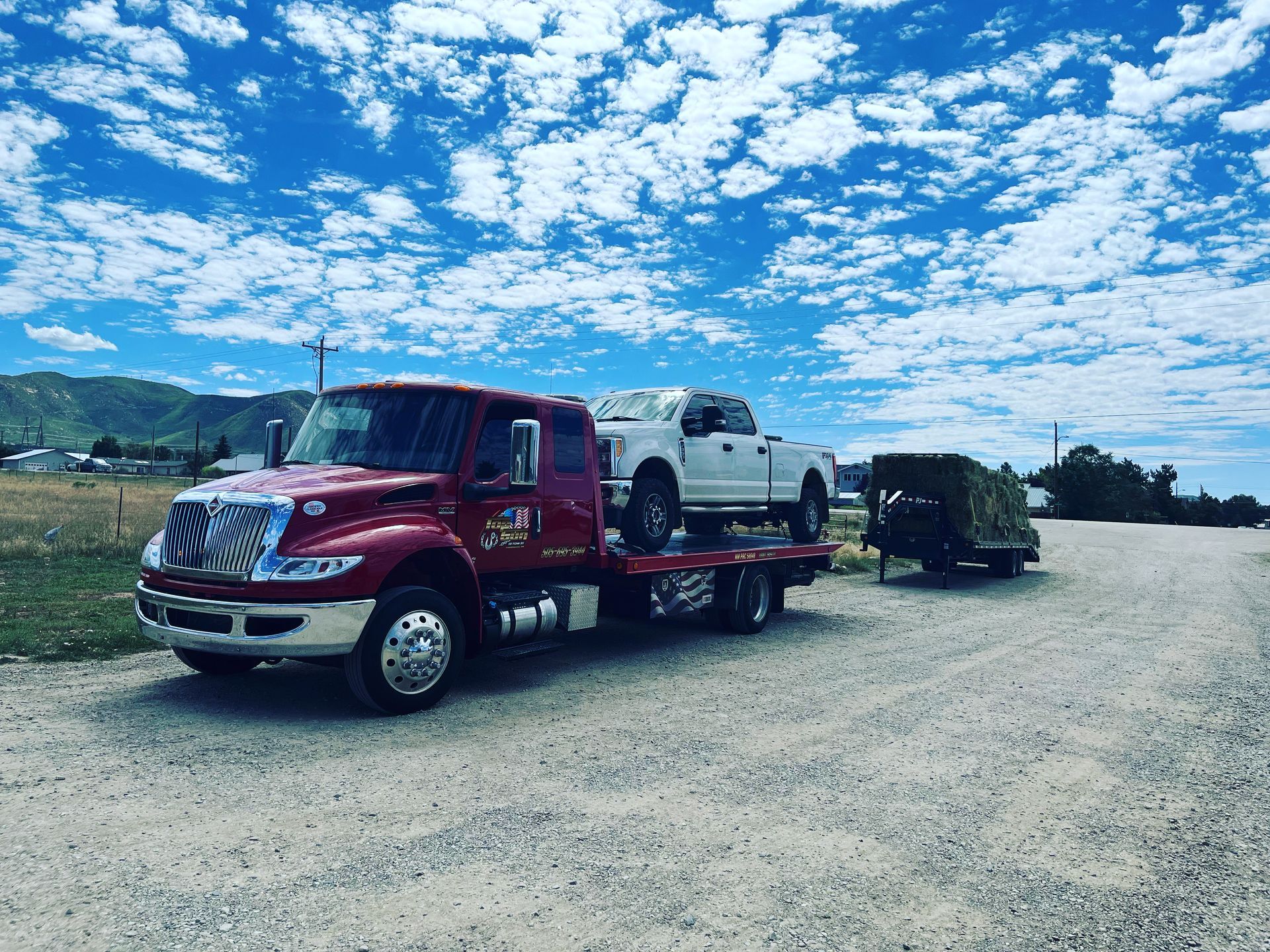 A red tow truck is towing a white truck on a trailer.