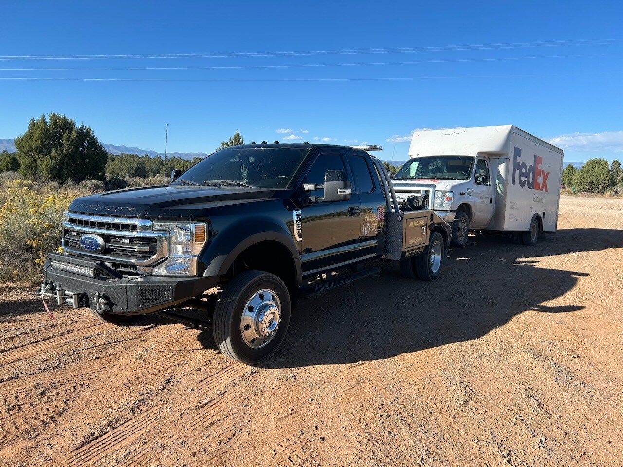 A black truck is towing a fedex trailer on a dirt road.