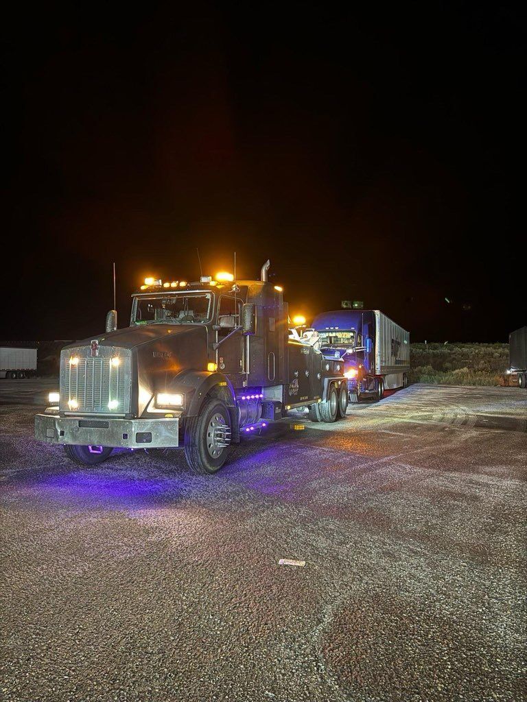 Two semi trucks are parked in a gravel lot at night.