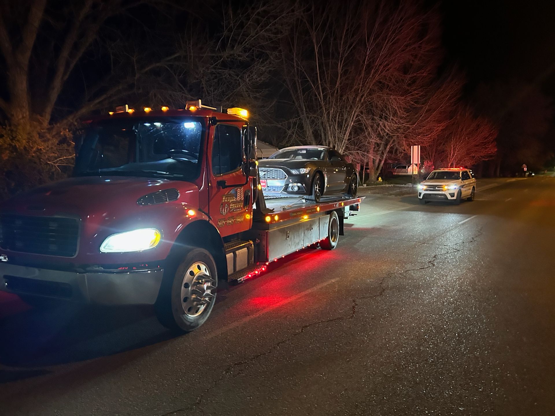 A tow truck is towing a car down a street at night.