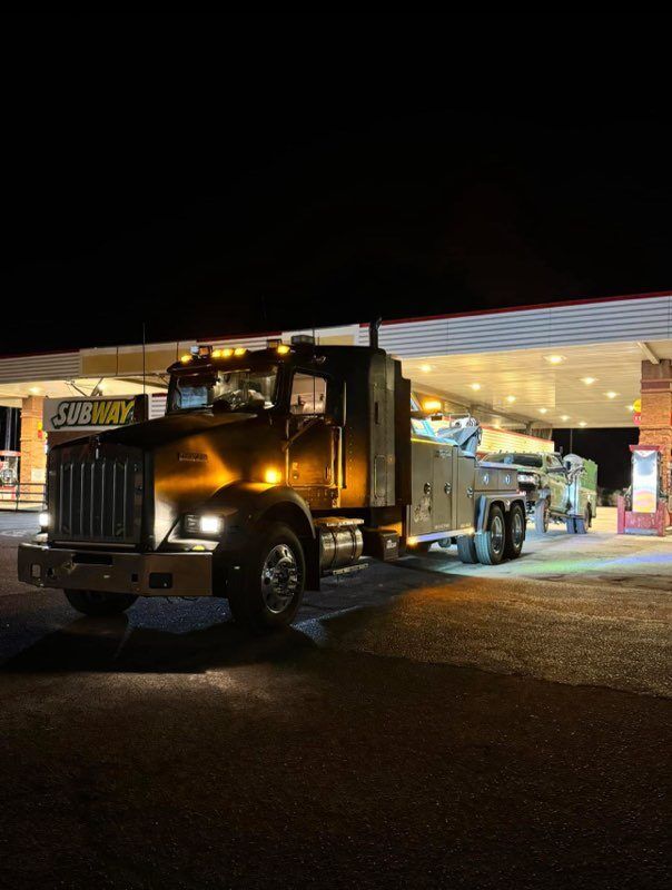 A tow truck is parked in front of a gas station at night.