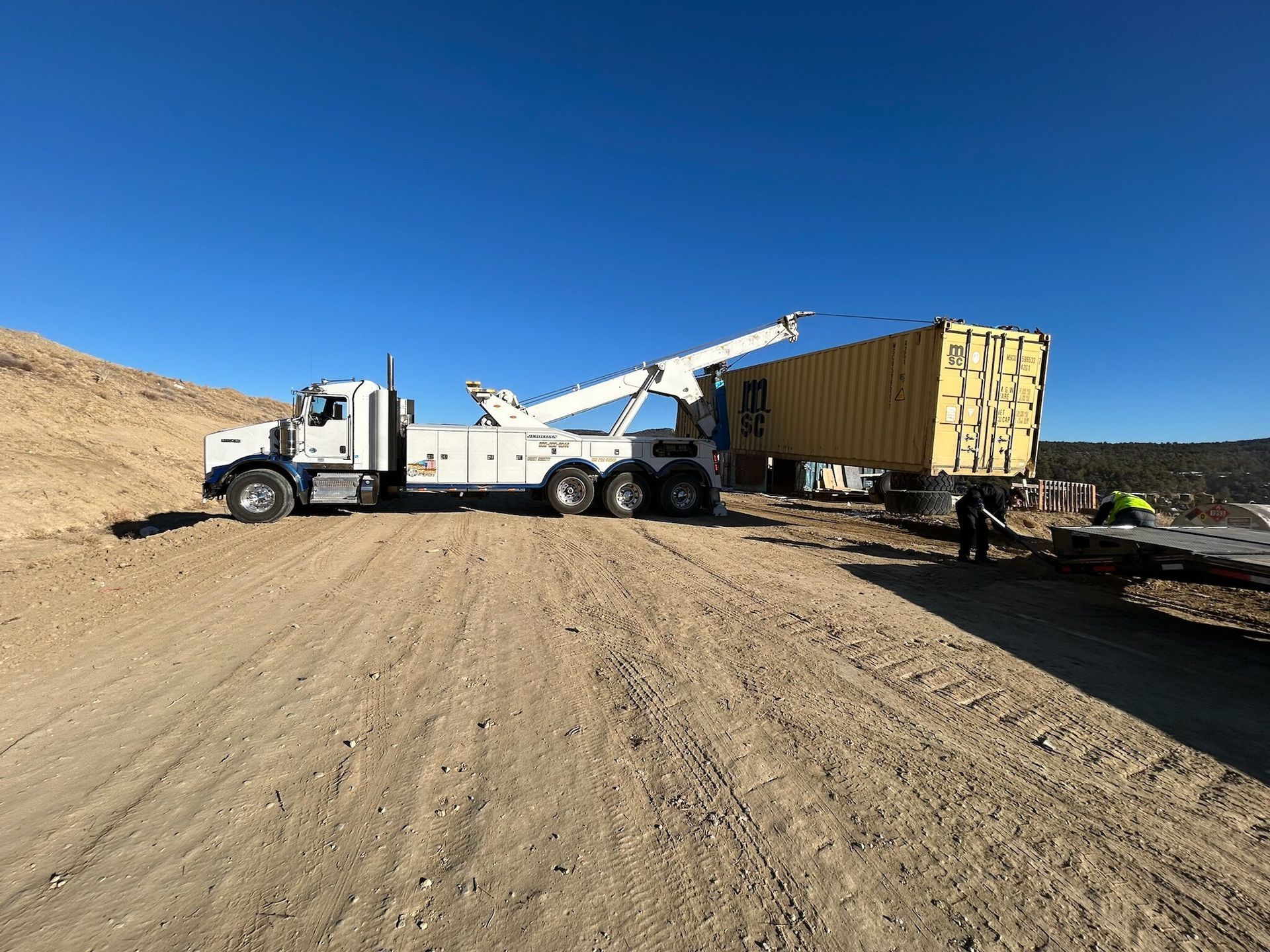 A tow truck is towing a yellow container down a dirt road.