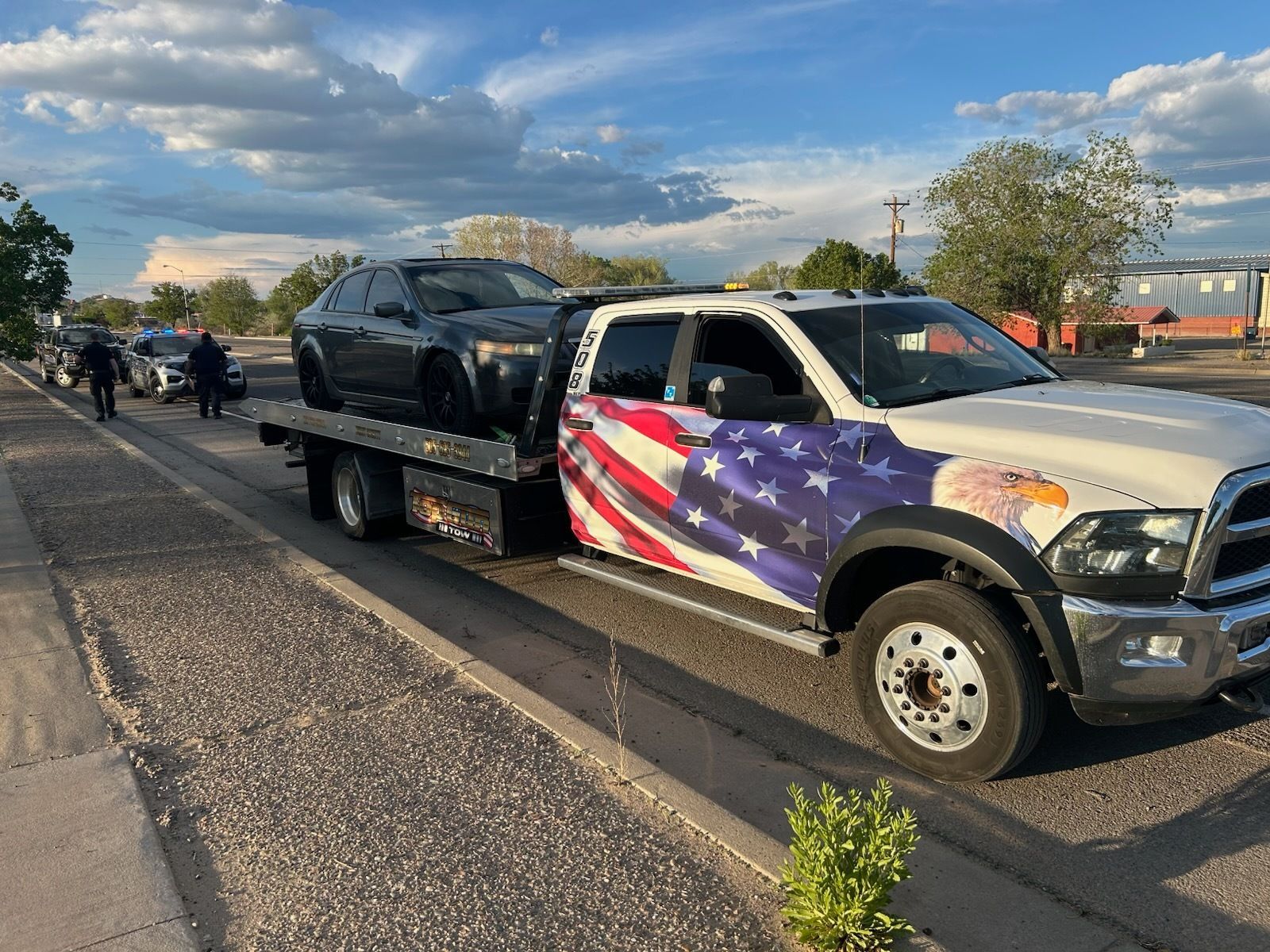 A tow truck with a car on the back is parked on the side of the road.