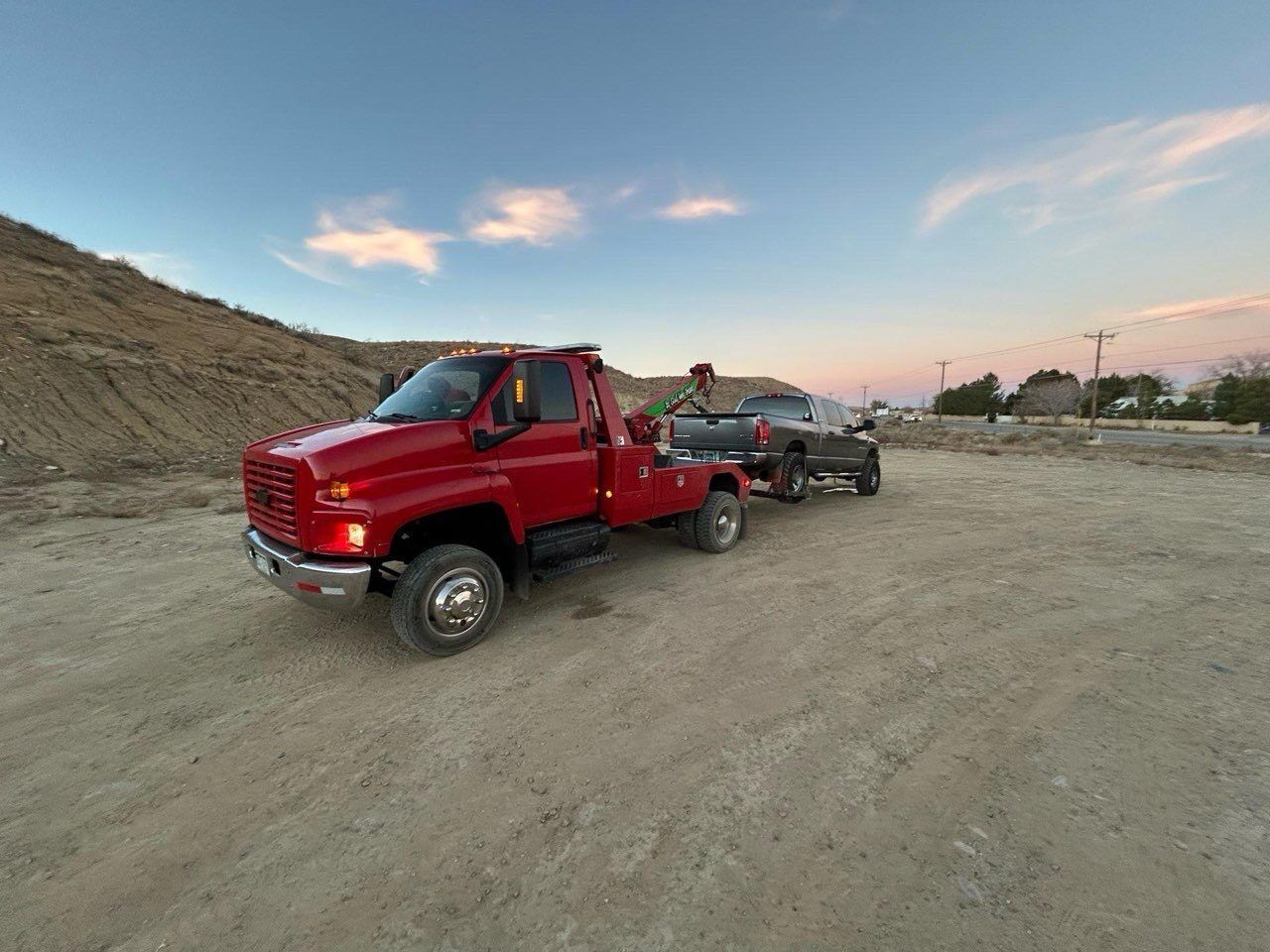 A red tow truck is towing a black truck in a dirt field.