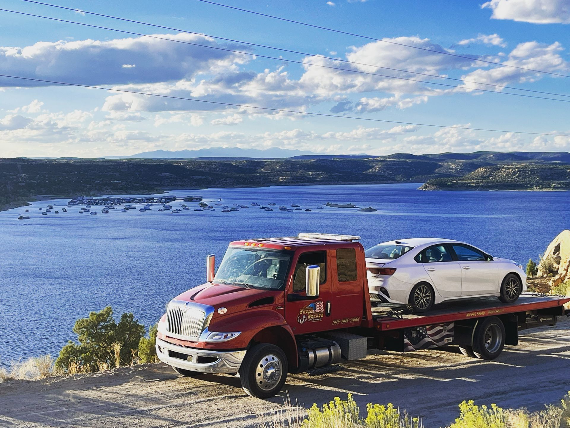 A tow truck with a car on the back is parked on the side of a road next to a lake.