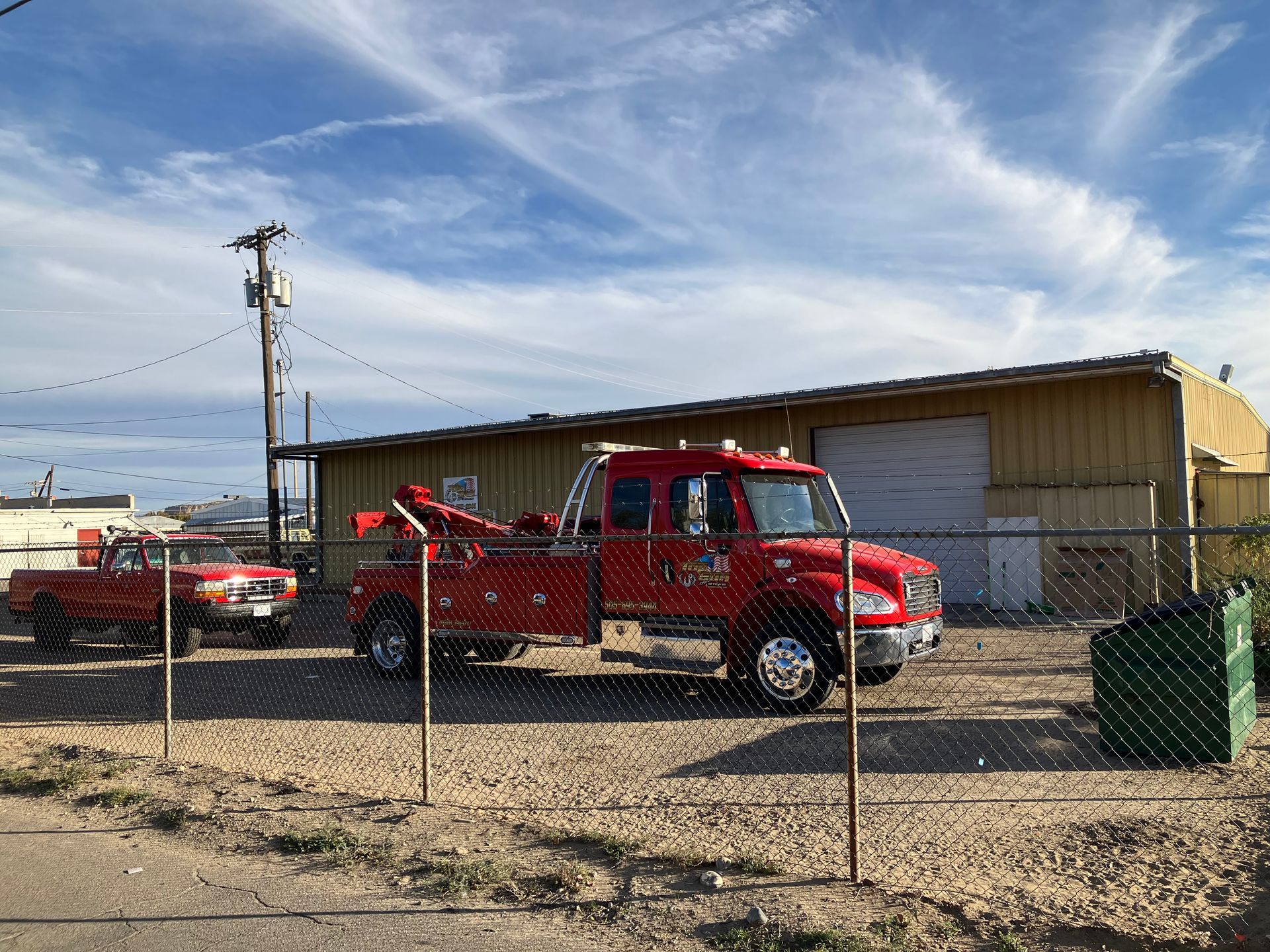 A red tow truck is parked in front of a building behind a chain link fence.
