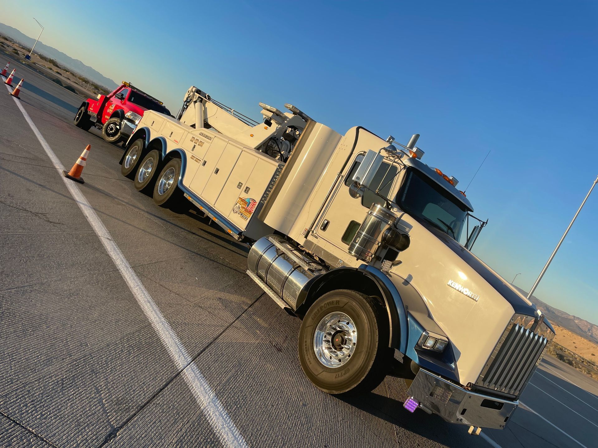 A white tow truck is parked on the side of the road next to a red truck.