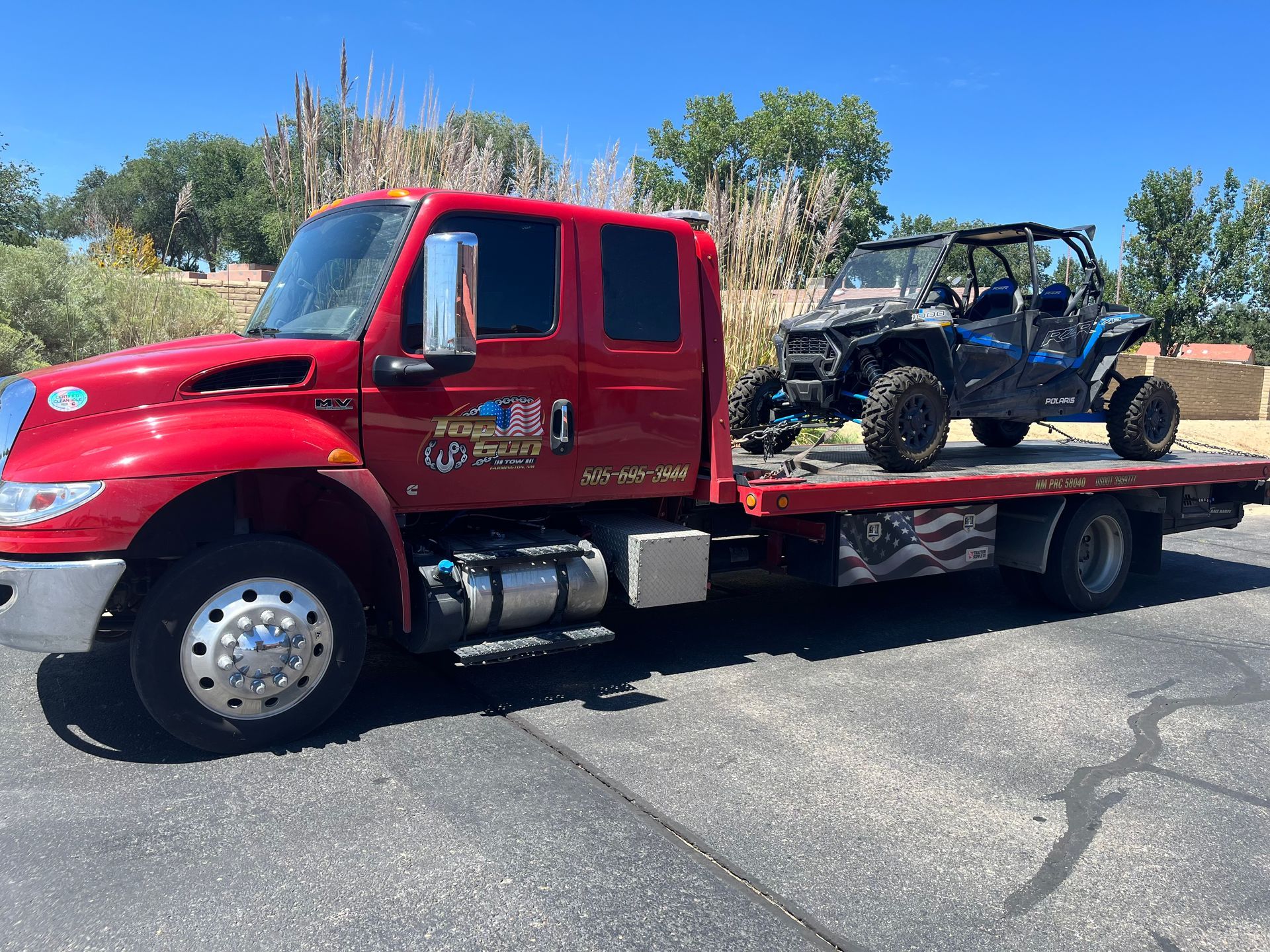 A red tow truck is carrying a four wheeler on the back of it.