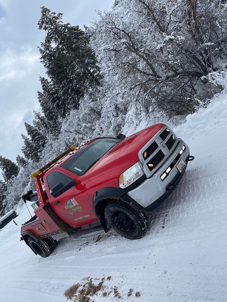 A red tow truck is driving down a snowy road.
