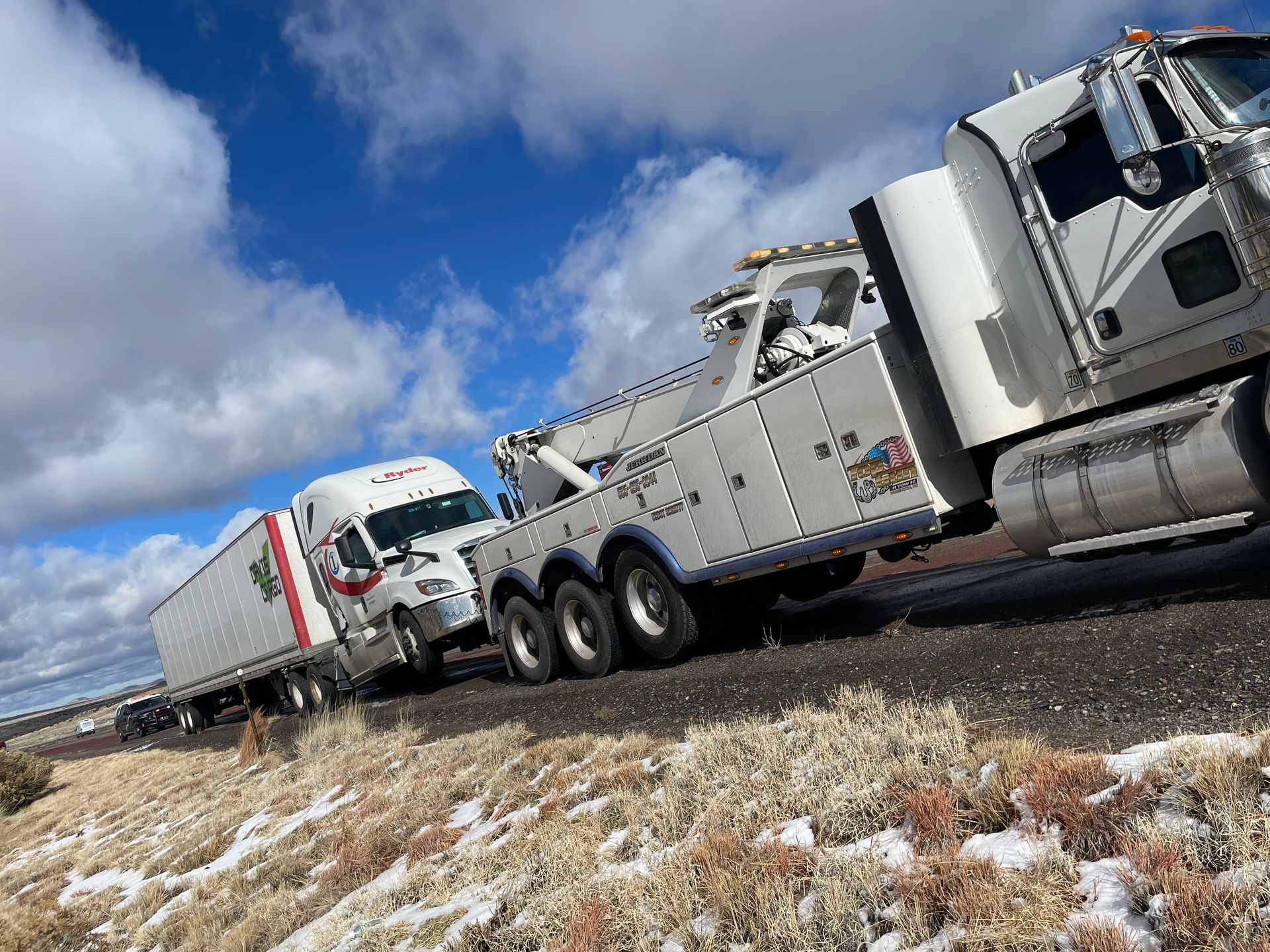 A tow truck is towing a semi truck down a road.