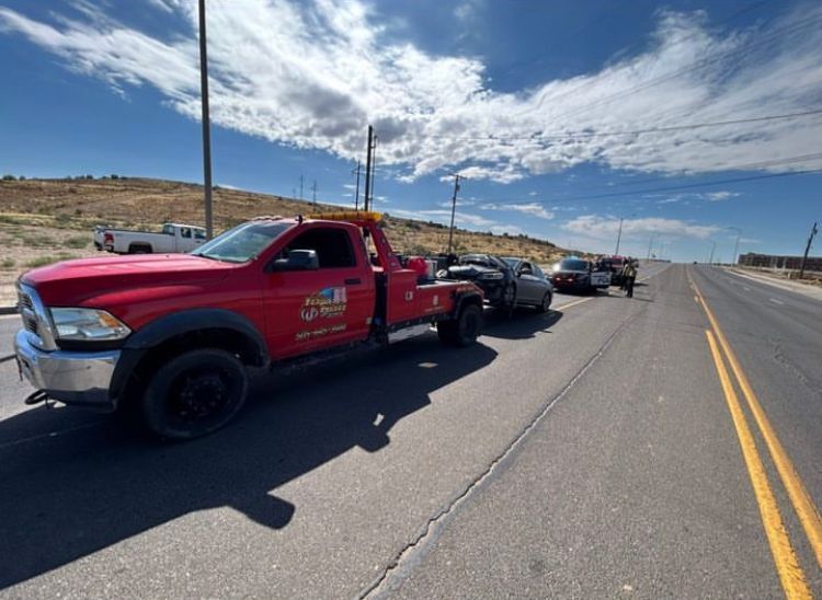 A red tow truck is towing a car on the side of the road.