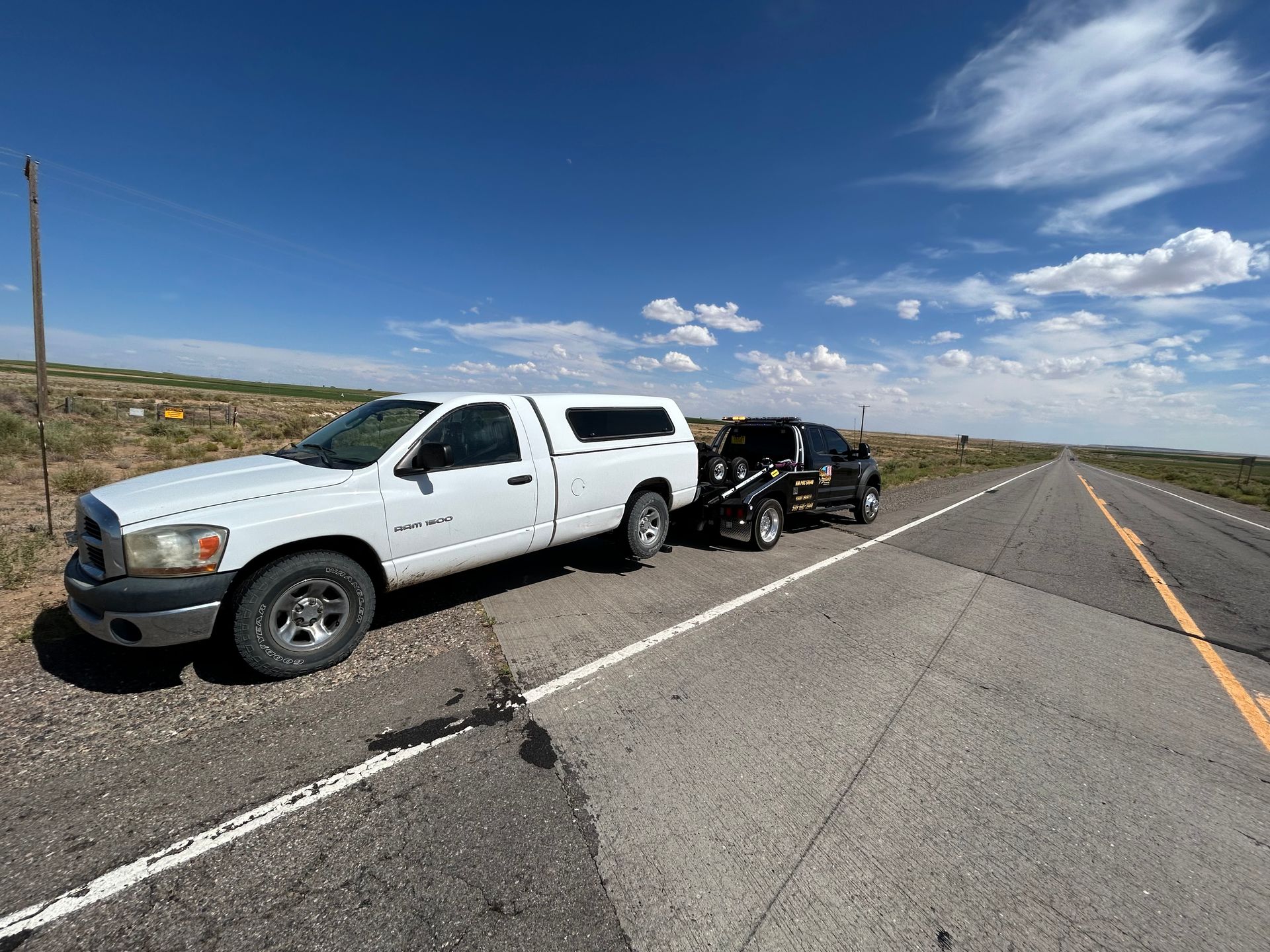 A white truck is towing a black truck down a highway.