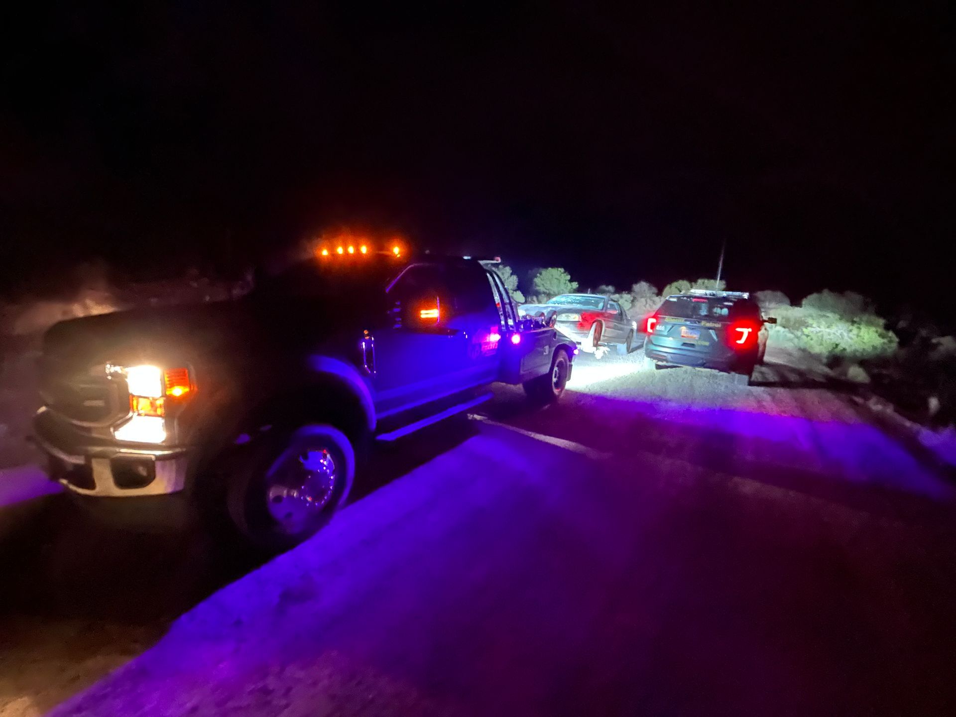 A group of cars are parked on the side of a road at night.