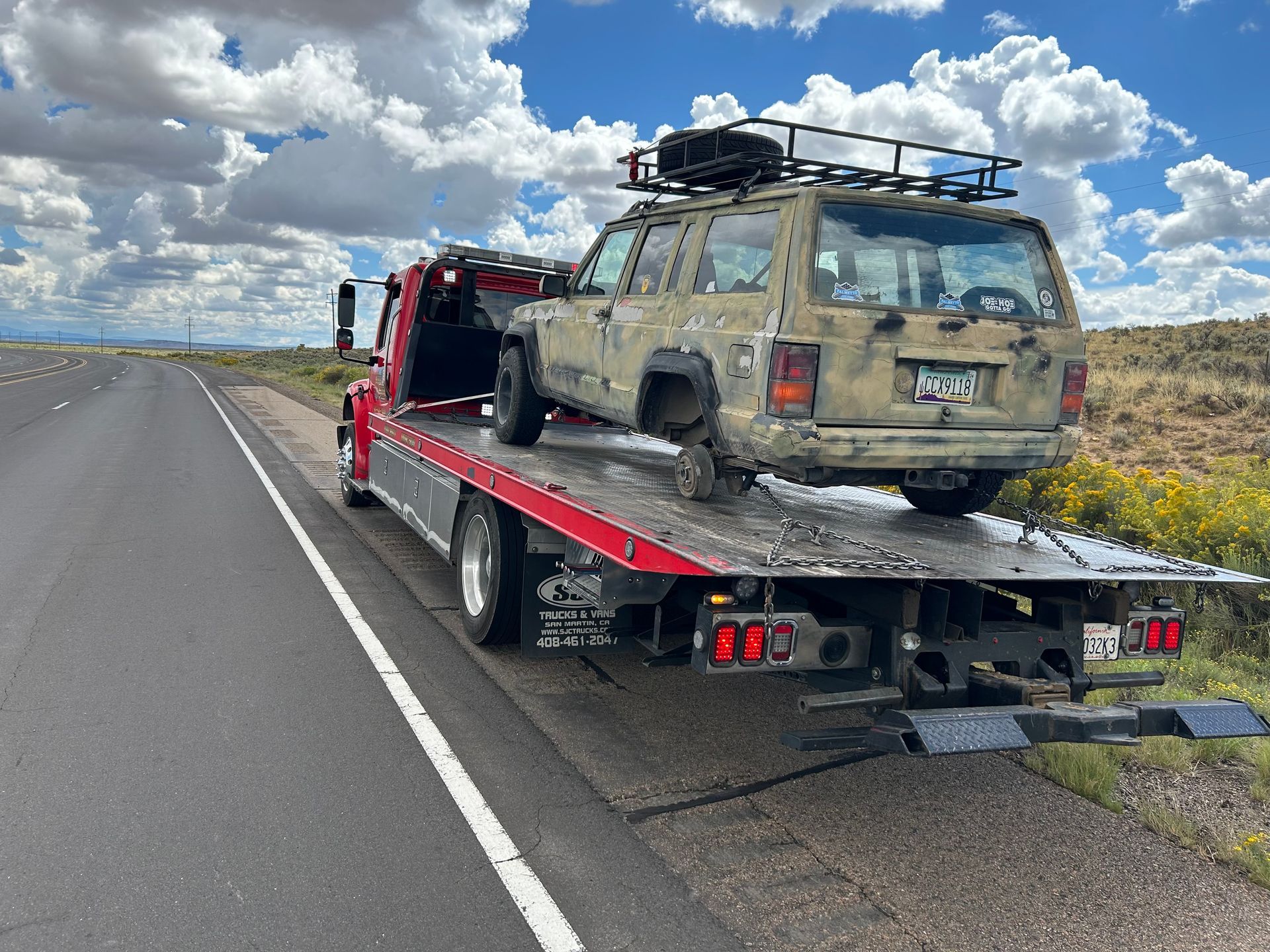 A jeep is being towed by a tow truck on the side of the road.