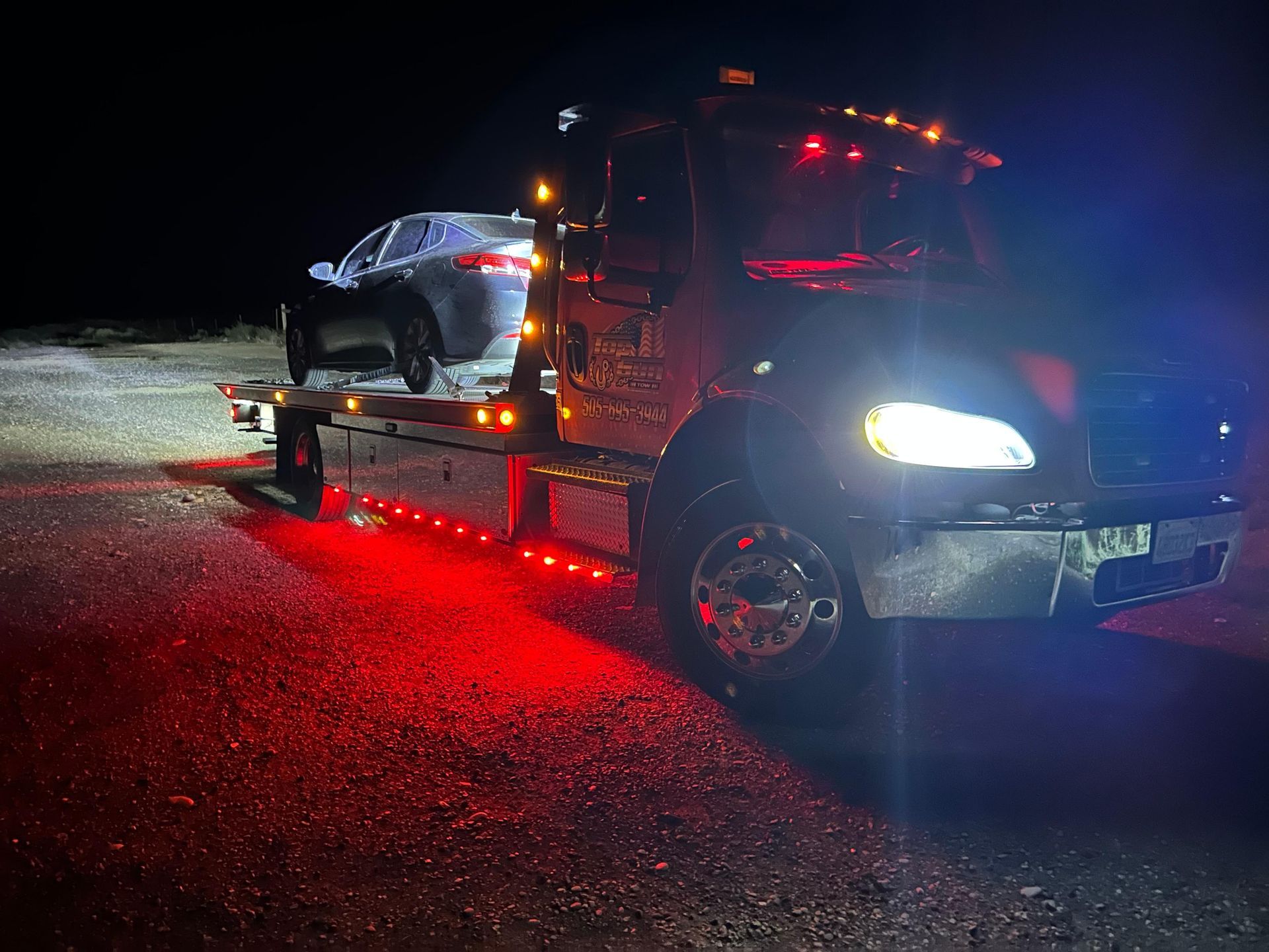 A tow truck is towing a car at night.