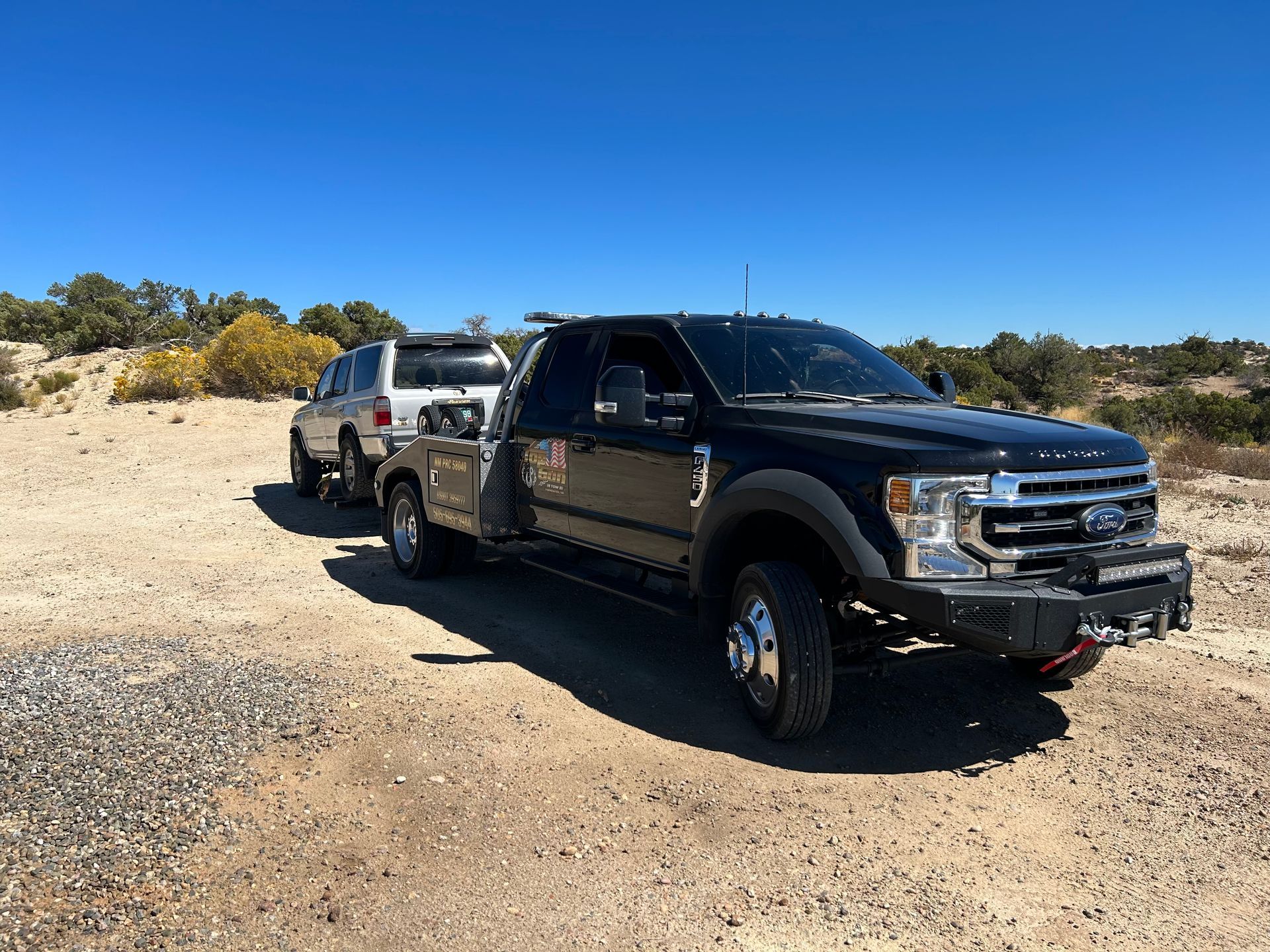A black truck is parked next to a white truck on a dirt road.