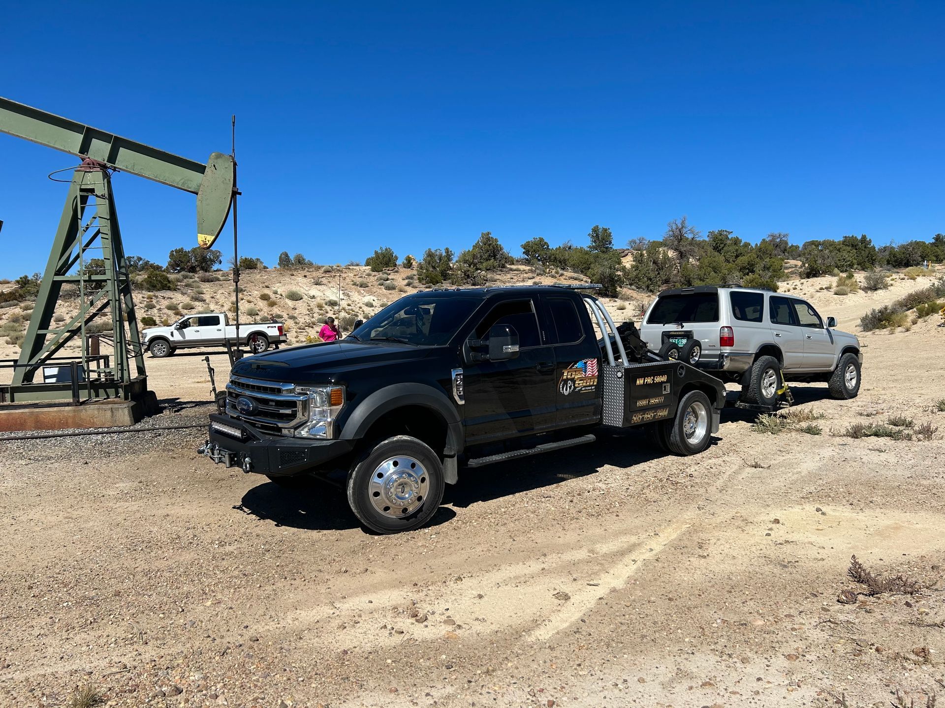 A black tow truck is towing a white truck in a dirt field.