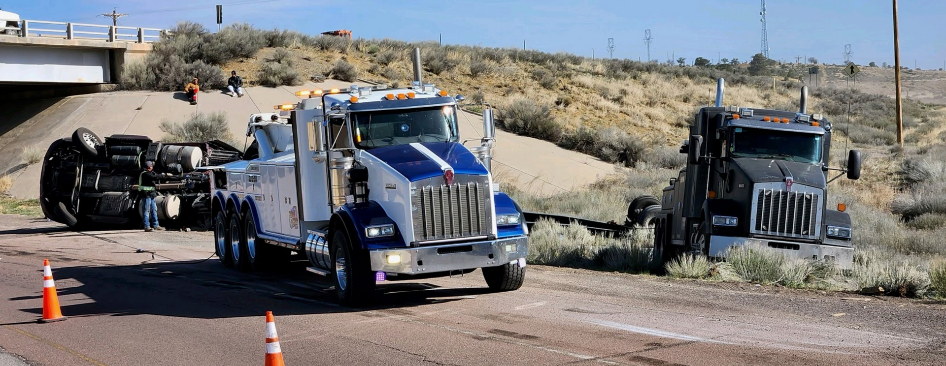 A tow truck is towing a truck that has rolled over on the side of the road.