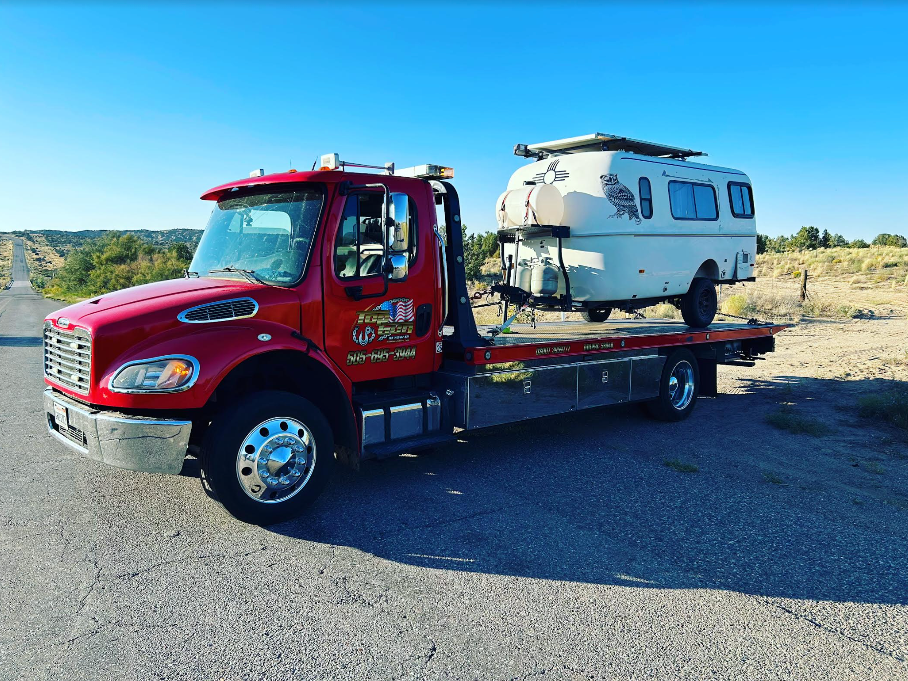A red tow truck is towing a white rv down the road.