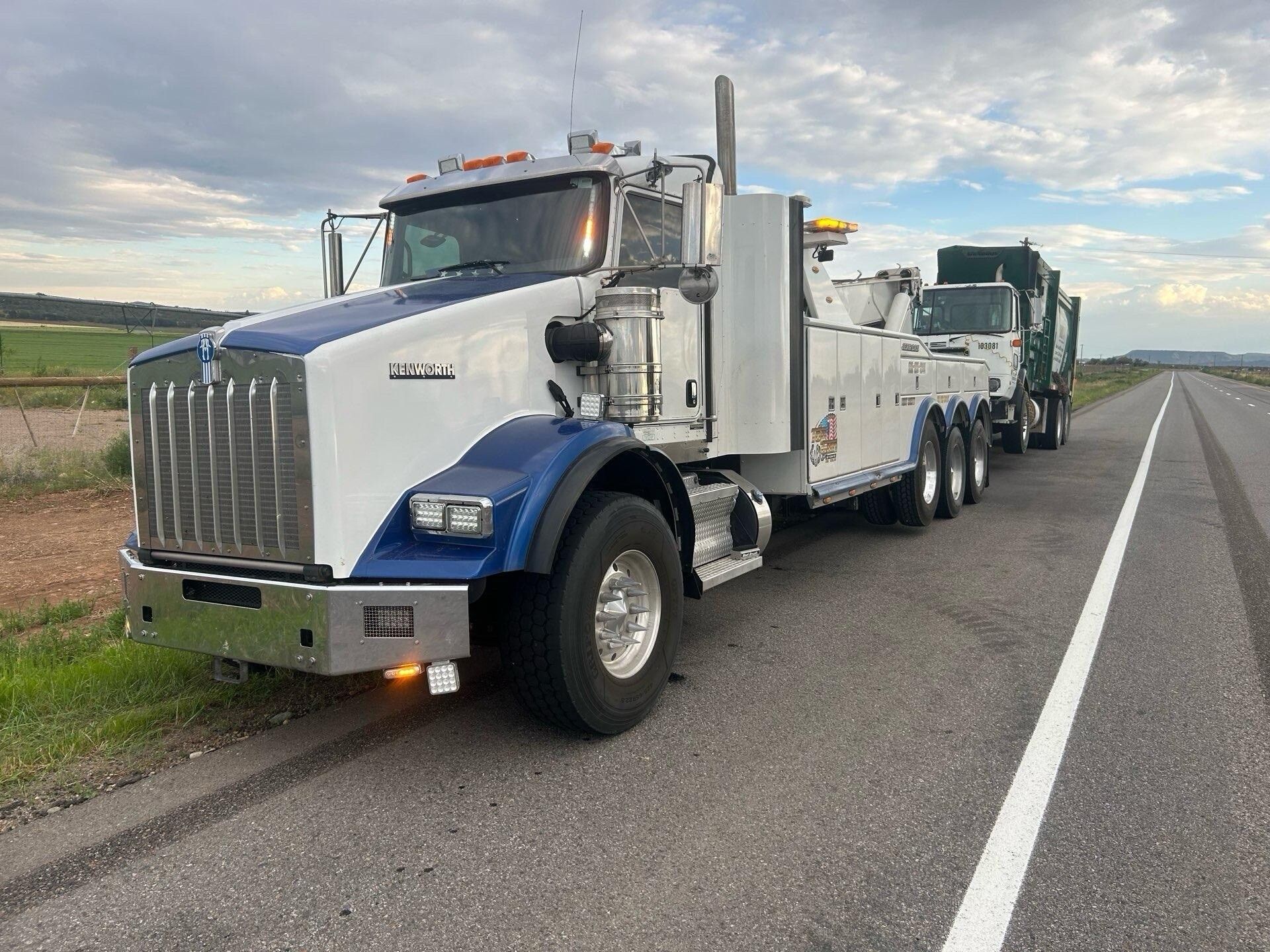 A white and blue tow truck is parked on the side of the road.