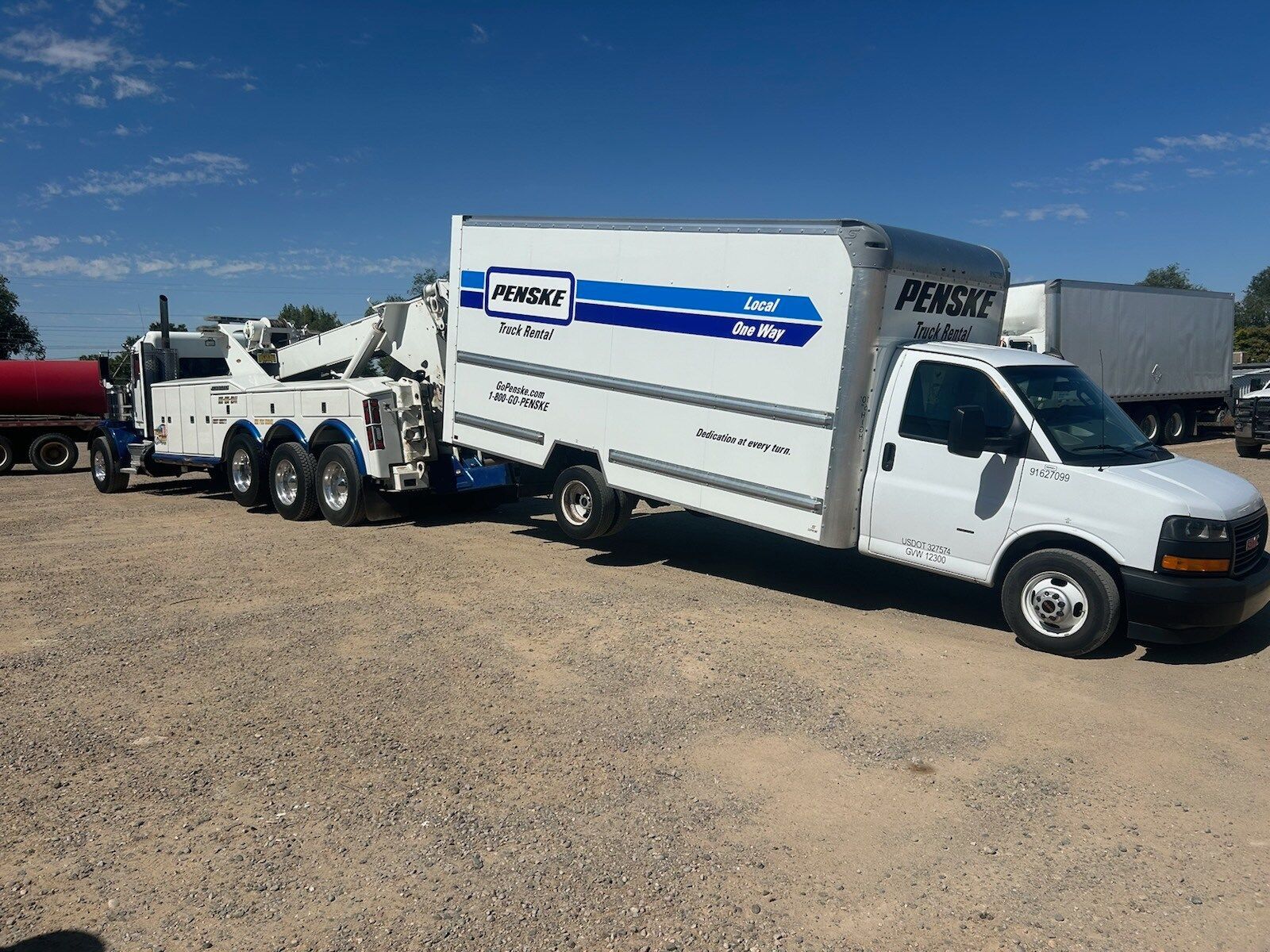 A white truck with a tow truck attached to it is parked in a gravel lot.