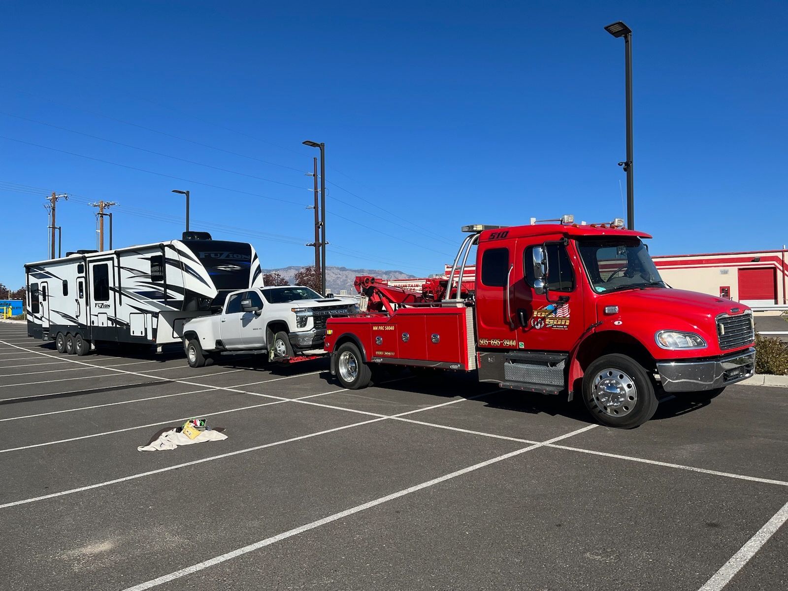 A red tow truck is towing a trailer in a parking lot.