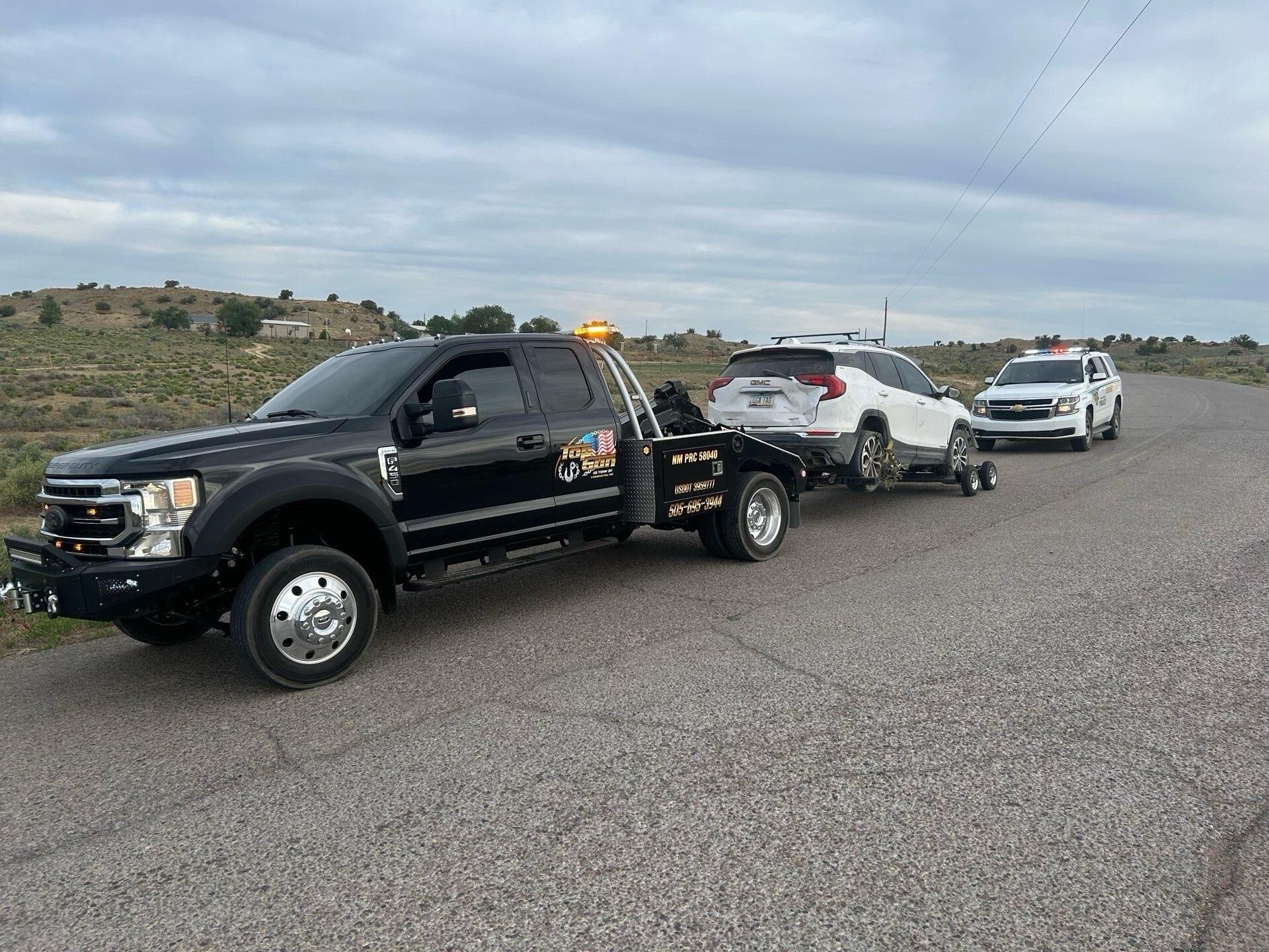 A black tow truck is towing a white suv down a road.