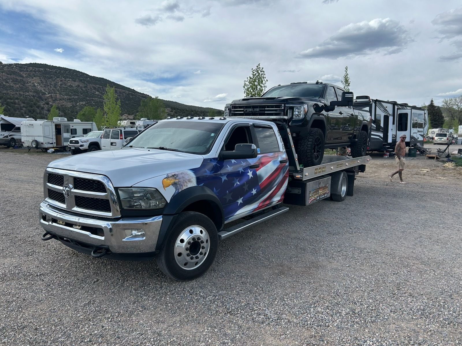 A tow truck with an american flag painted on the side is carrying a rv.