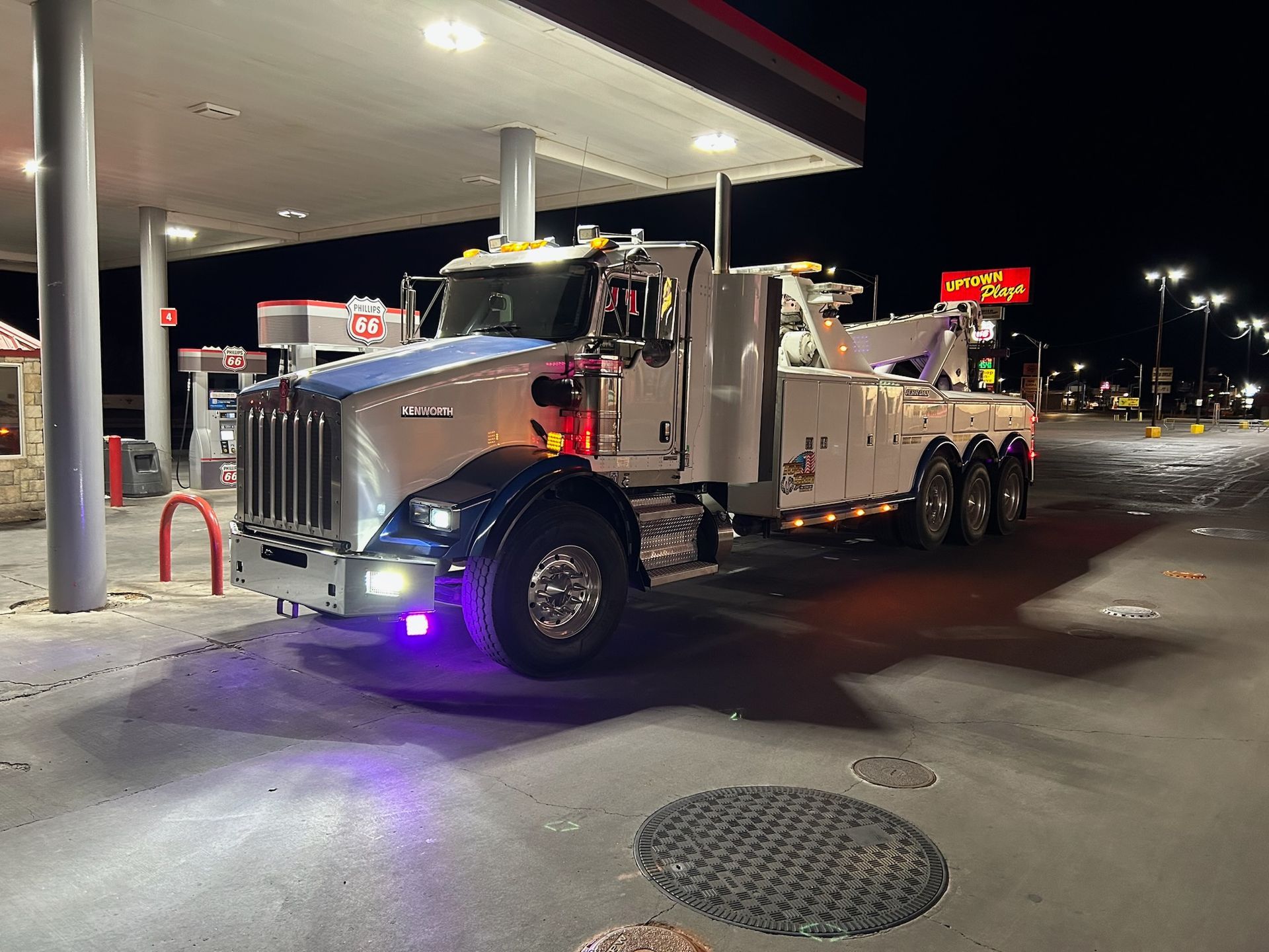 A tow truck is parked in front of a gas station at night.